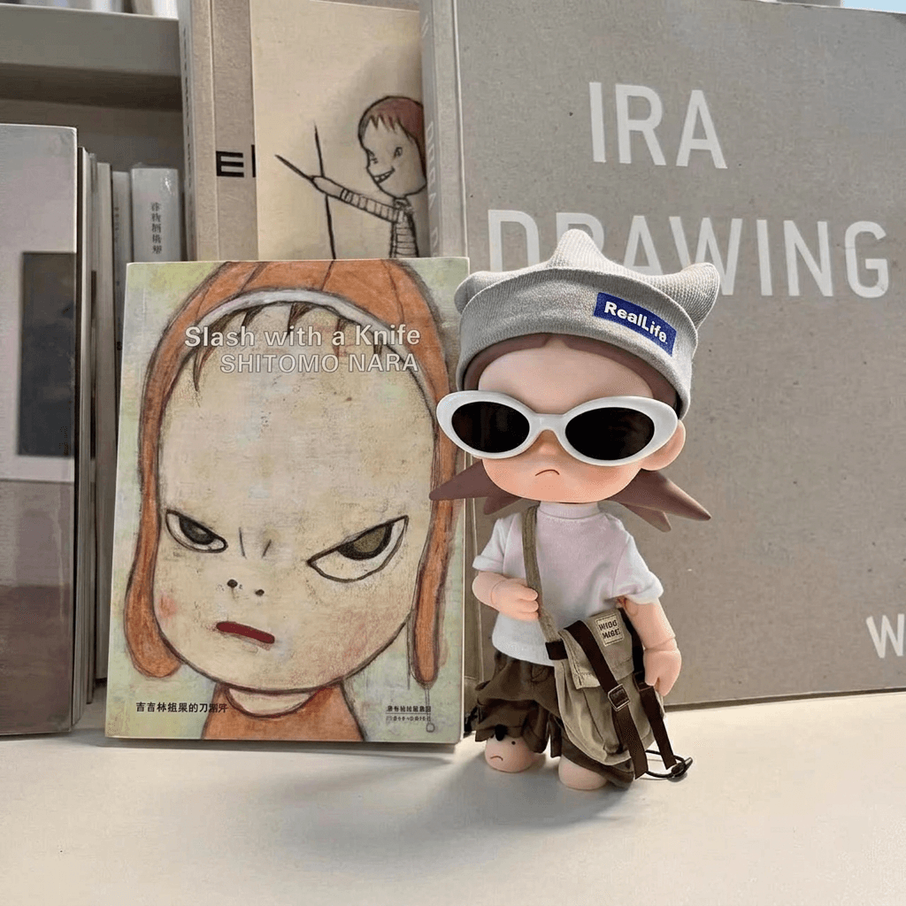 A stylish toy figure wearing sunglasses next to art books