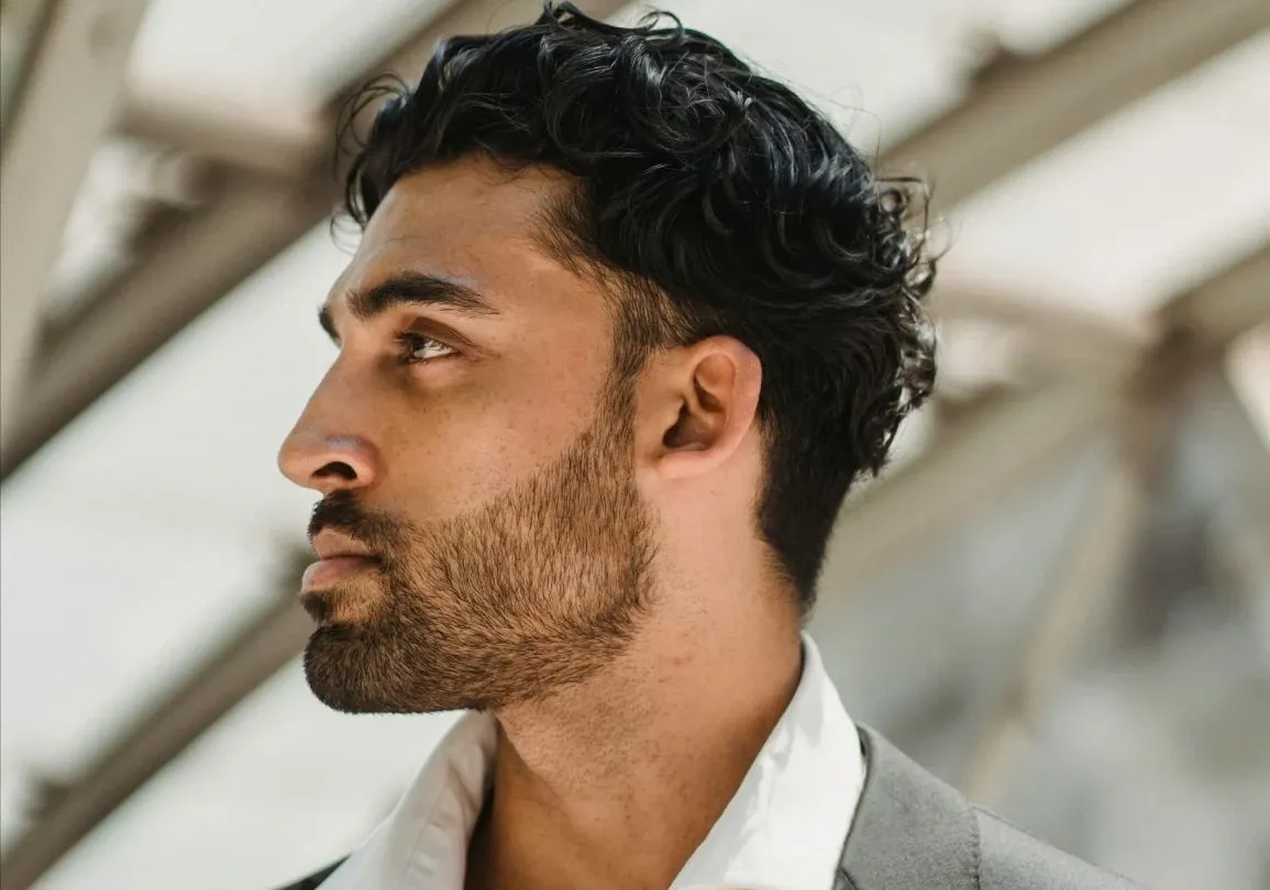 A side profile portrait of a bearded man with a modern architectural background