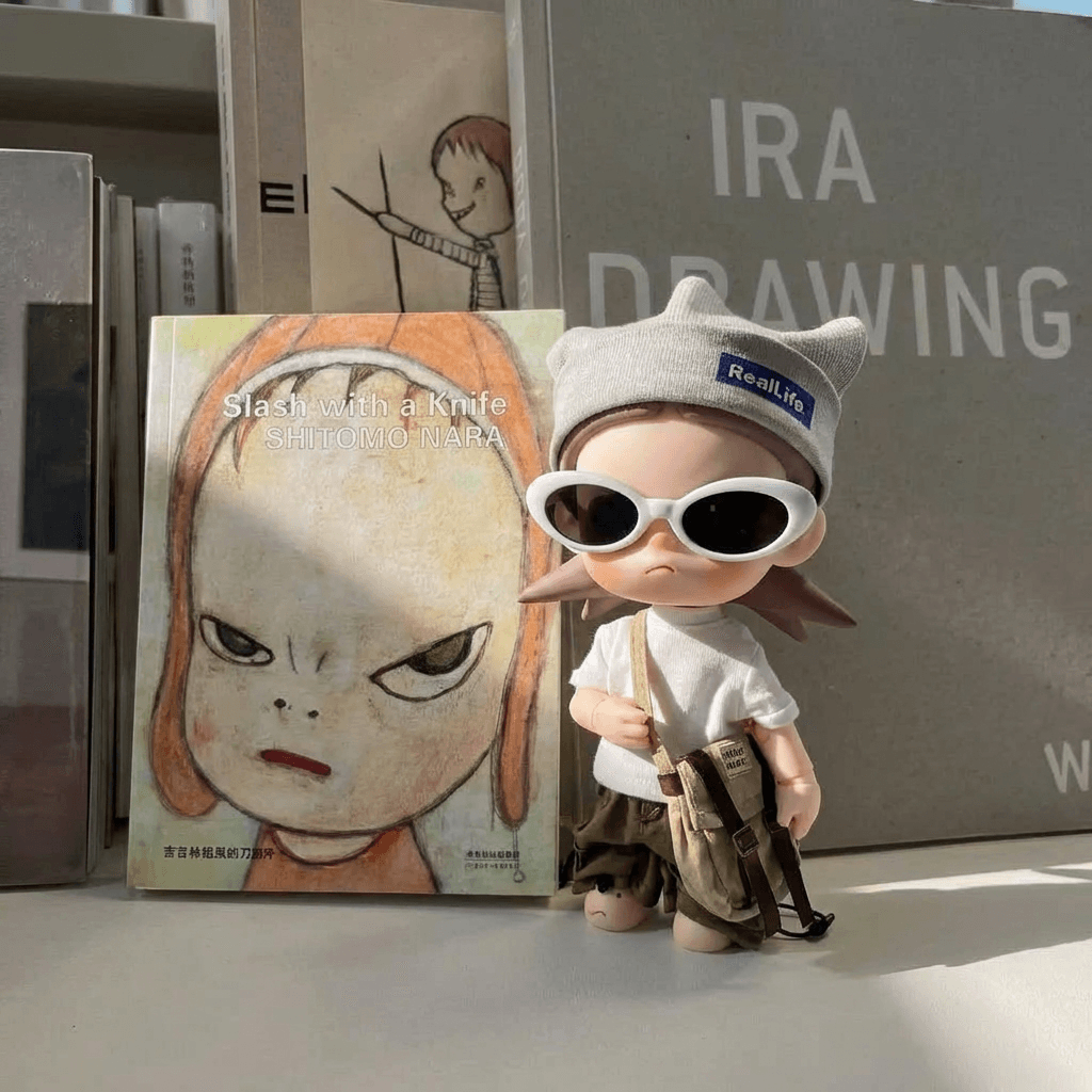 A toy figure displayed with an art book in front of a shelf