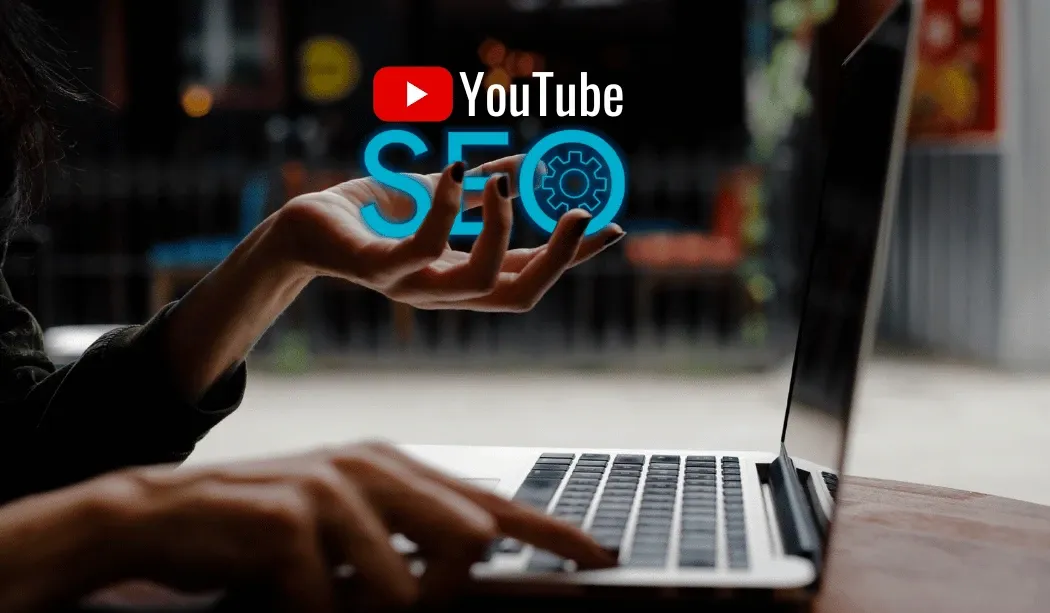 A hand holding the text “YouTube SEO” beside a laptop, symbolizing video search engine optimization